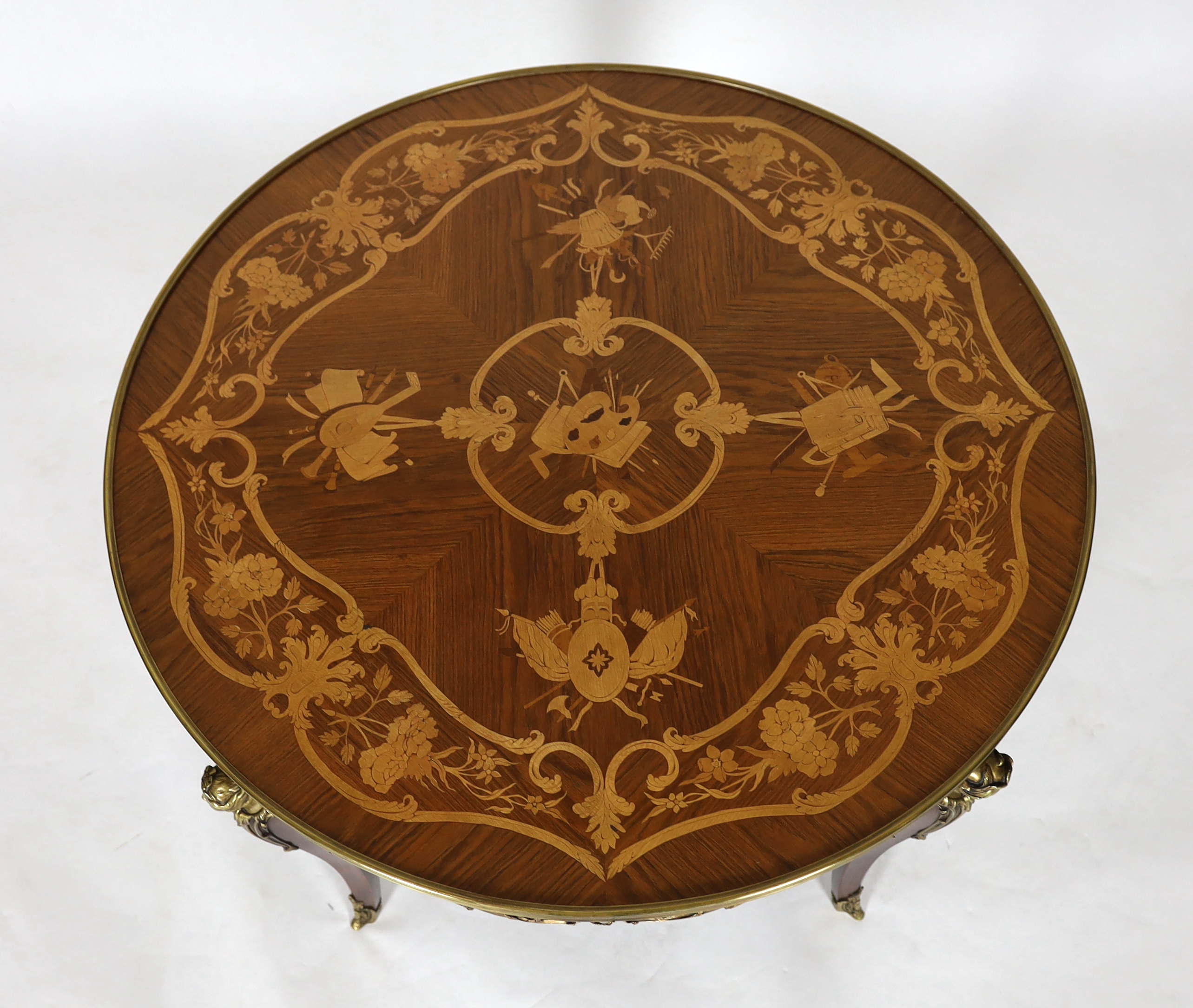 A Louis XVI style ormolu mounted marquetry centre table, decorated with musical, agricultural and arts related trophies within a band of flowers, the circular top over a scroll mounted frieze with classical mask headed c